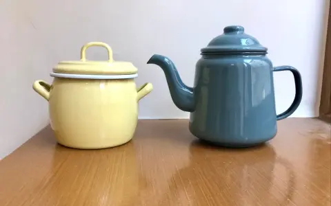 En gul gryta och en blå kaffepanna i emalj, liknande en klassisk kockums kaffepanna, står på ett träbord.