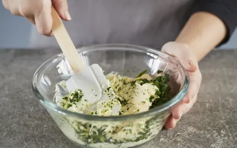 Hände mischen Kräuter und Butter in einer Schüssel. Perfekt, um Kräuterbutter selber zu machen.