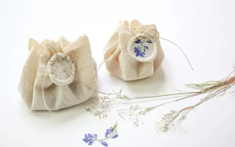 Dos pequeños paquetes de tela rústica, atados con hilo y sellados con cera, decorados con flores secas. Son detalles de boda originales hechos a mano, perfectos para un toque natural.