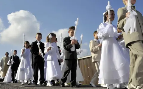 Kinder in festlicher Kleidung, was zieht man zur Kommunion an? Mädchen in weißen Kleidern, Jungen in Anzügen, alle tragen Kerzen.