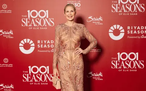 A woman in a sparkling celio saab gown poses at an event with "1001 Seasons of Elie Saab" branding.