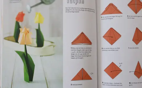 Vackra vika pappersblommor i form av tulpaner, en klassiker inom origamikonsten. En orange tulpan i förgrunden, med en röd och en gul i bakgrunden.