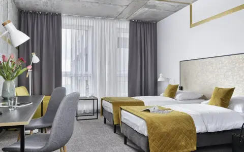 Pokój hotelowy z dwoma łóżkami, biurkiem i kwiatami. Idealne miejsce na wcześniejsze zameldowanie w hotelu.