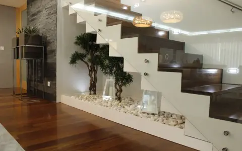 Elegante subida de escalera interior con plantas decorativas y piedras blancas.