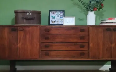 Mobile legno scolorito con cassetti e ante, decorato con una valigia vintage, cornici con farfalle e un vaso di fiori.
