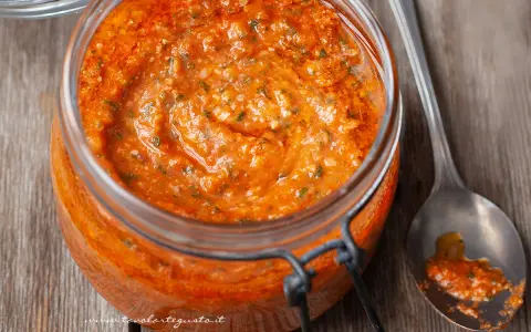 Vaso di pesto alla trapanese, un condimento rosso vivo con pomodori, mandorle e basilico, pronto per essere gustato.