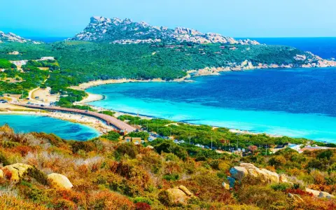 Vacker kustlinje med turkost vatten, en bro och gröna kullar. En dröm för en **Sardinien resa**.