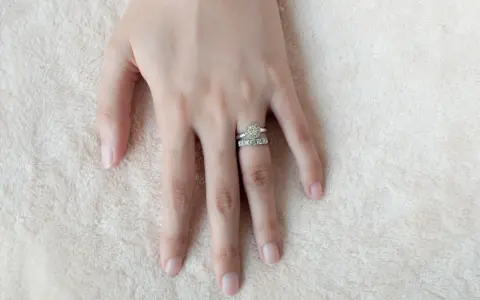 Mano femminile con due anelli scintillanti, uno con un grande diamante centrale e l'altro con pietre più piccole. Il dito anulare è il posto tradizionale dove si mette l'anello di fidanzamento donna.