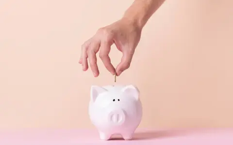 Mano inserta moneda en alcancía blanca, simbolizando cómo empezar una cuenta de ahorro.