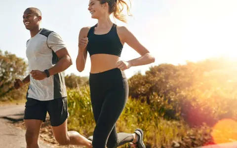 Ein Mann und eine Frau joggen lachend auf einem Feldweg. Die Sonne scheint, und die Atmung beim Joggen ist gleichmäßig und tief.