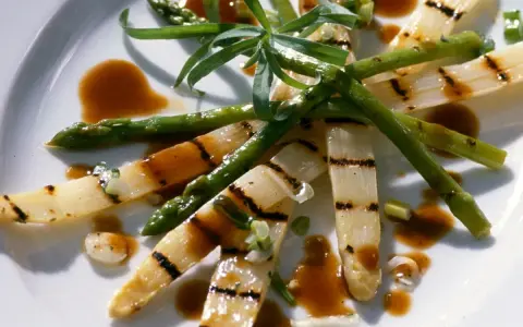 Gegrillter Spargel auf einem Teller, mit einer würzigen Sauce beträufelt und garniert mit frischen Kräutern.