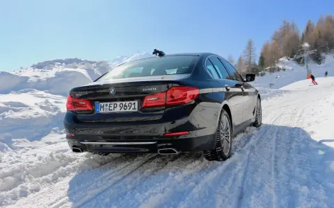 Schwarzer BMW 540i G30 fährt durch tiefen Schnee auf einer Skipiste, bergauf mit Skilift im Hintergrund.