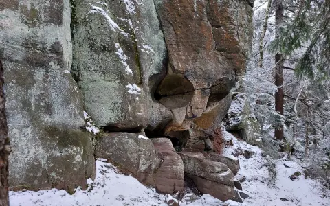 Skalna czaszka w zimowym lesie, z lodem i śniegiem na skałach i drzewach.