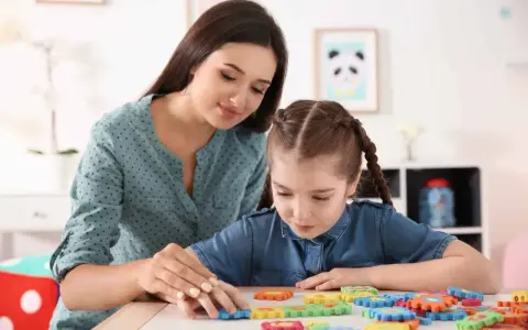 Terapeuta pomaga dziecku z niepełnosprawnością intelektualną w stopniu lekkim układać kolorowe puzzle.