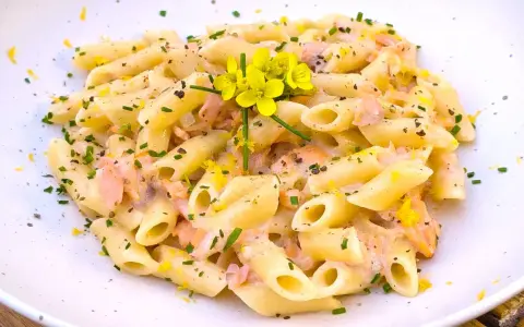 Pasta penne cremosa con trozos de salmón rosado, ralladura de limón y flores amarillas.