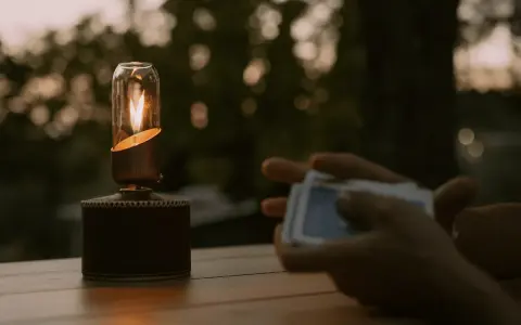 En gasollampa lyser varmt på ett träbord medan någon håller en kortlek.