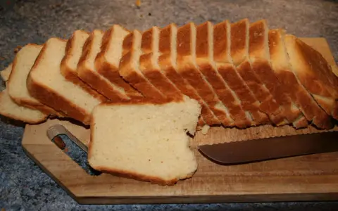 Tranches de pâte à pain de mie dorées et moelleuses, prêtes à être dégustées sur une planche en bois avec un couteau.