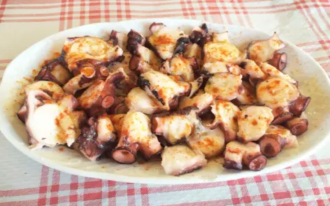 Pulpo a la gallega servido en plato blanco sobre mantel a cuadros rojos y blancos.