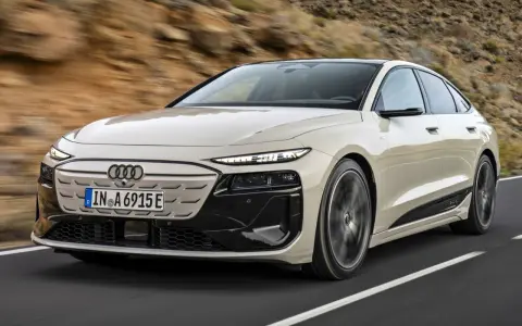 Jasnoszary Audi A6 e-tron z czarnymi akcentami jedzie po drodze.