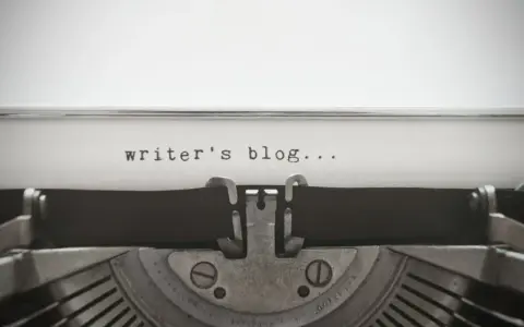 Maszyna do pisania z napisem "writer's blog..." na papierze. Idealny przykład wpisu na bloga po angielsku.