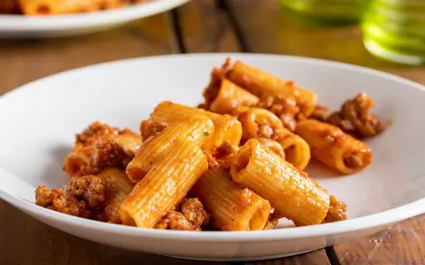Rigatoni conditi con un ricco ragù di salsiccia, serviti su un piatto bianco.