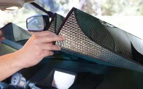 Mani che posizionano un parasole riflettente sul cruscotto per proteggere l'auto dal sole.