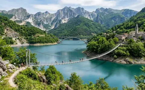 Un ponte sospeso attraversa il lago di Vagli, con montagne imponenti e un borgo pittoresco sullo sfondo.