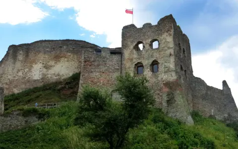 Ruiny zamku Czorsztyn na wzgórzu, z polską flagą powiewającą na wieży.