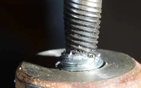 Uszkodzona śruba w aluminiowej obudowie. Widoczne ślady po próbie wykręcenia urwanej śruby z aluminium.
