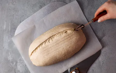Ein Laib Brot wird mit einem Bäckermesser eingeschnitten, bereit zur Zubereitung mit Sauerteigpulver.