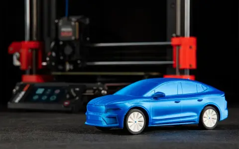 Niebieski model samochodu, gotowy do drukowania, stoi przed drukarką 3D.
