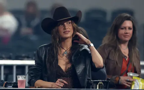 Mujer con sombrero tejano y chaqueta de cuero, disfrutando de un evento. Se aprecian otros tipos de tejanos en el público.