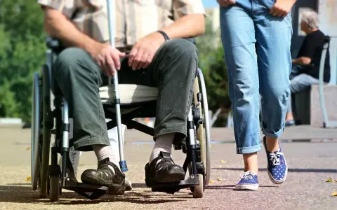 Osoba na wózku inwalidzkim z laską obok idącej osoby. Ulga na śmieci dla niepełnosprawnych to ważny temat.
