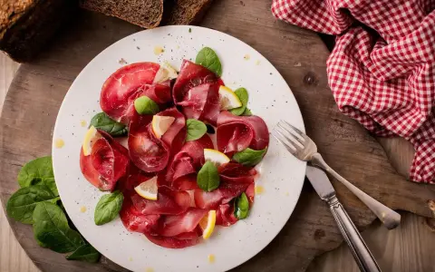 Bresaola affettata finemente, guarnita con spinacini freschi e spicchi di limone. Un'idea semplice su come condire la bresaola per un antipasto leggero.