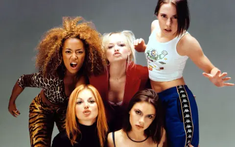 Medlemmar av Spice Girls poserar energiskt. Mel B i leopardmönster, Emma B i rött, Mel C i Buzz Lightyear-linne, Geri H med rött hår och Victoria B med mörkt hår.
