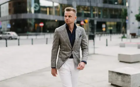 Elegancki mężczyzna w szarej marynarce w kratę i białych spodniach. Idealne połączenie, jeśli zastanawiasz się, jakie spodnie do szarej marynarki pasują.