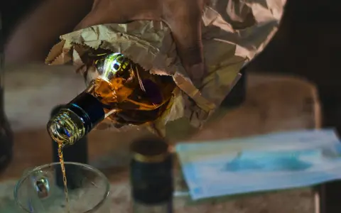 Ręka trzyma butelkę z alkoholem, z której nalewany jest płyn do szklanki. To może być początek drogi do dawki śmiertelnej alkoholu.