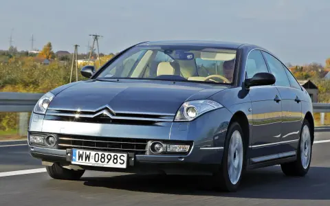 Elegancki Citroën C6 w kolorze granatowym jedzie po drodze. Wnętrze z jasną tapicerką i kierowcą.