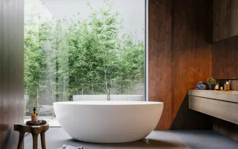 Mała łazienka w stylu spa z wolnostojącą wanną i widokiem na bambusowy ogród. Drewniane akcenty i kamienne płytki tworzą relaksującą atmosferę.