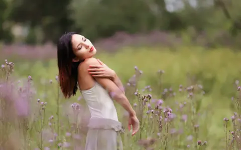Portrait en bokeh d'une femme aux yeux fermés, bras croisés sur la poitrine, dans un champ de fleurs sauvages mauves.