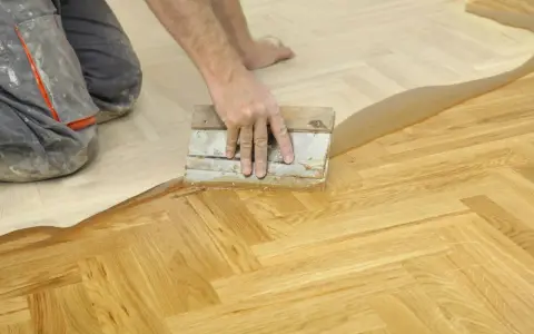Un artisan applique un produit sur un parquet en chevrons. Une étape essentielle pour la réparation parquet.