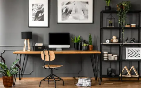 Arredamento studio casa: scrivania in legno con computer, sedia, piante e libreria nera piena di oggetti decorativi.