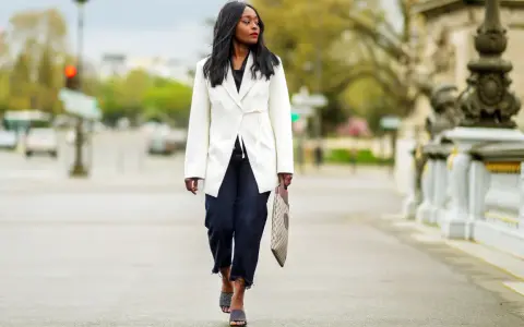Mujer con un look smart elegant, lleva un blazer blanco, jeans oscuros y sandalias de diseño.