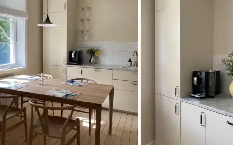 Ljust kök med träbord och stolar. Nya köksluckor ger ett fräscht intryck. Kaffemaskin och blommor på bänken.