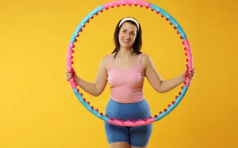 Uśmiechnięta kobieta z hula hop. Dowiedz się, jak dobrać hula hop do wzrostu, by ćwiczenia były efektywne i przyjemne.