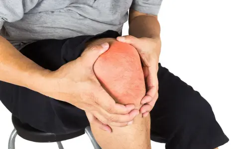 Ból w kolanie, zaznaczony czerwonym obszarem. Dłoń obejmuje bolące kolano.