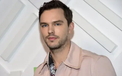 Nicholas Hoult, känd från filmer och tv-program, poserar framför en vit bakgrund med diagonala linjer.