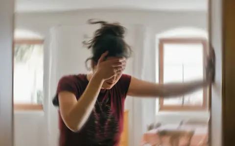 Kobieta z ręką na twarzy, doświadczająca zawrotów głowy. Padaczka alkoholowa co robić? Szukaj pomocy.