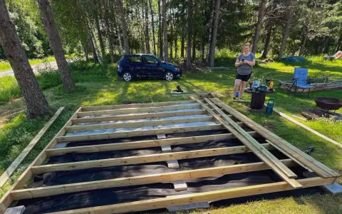 En kvinna förbereder sig för att skruva trall på en nybyggd altan i en lummig trädgård.