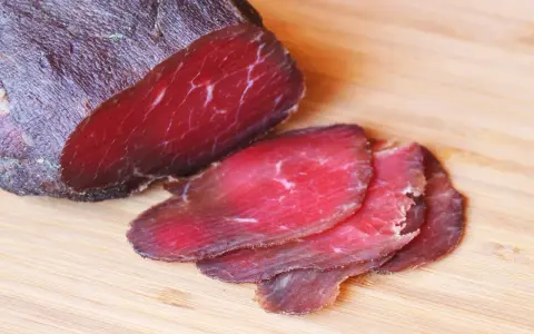 Bresaola co to? Ciemnoczerwone, cienko pokrojone plastry suszonej wołowiny na desce.